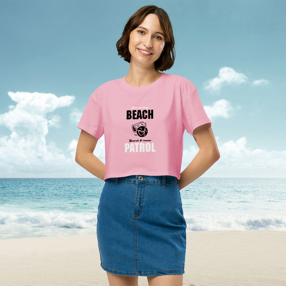 Woman wearing a pink t-shirt with 'Beach Patrol' text and retro hearts shades graphic design posing on a beach