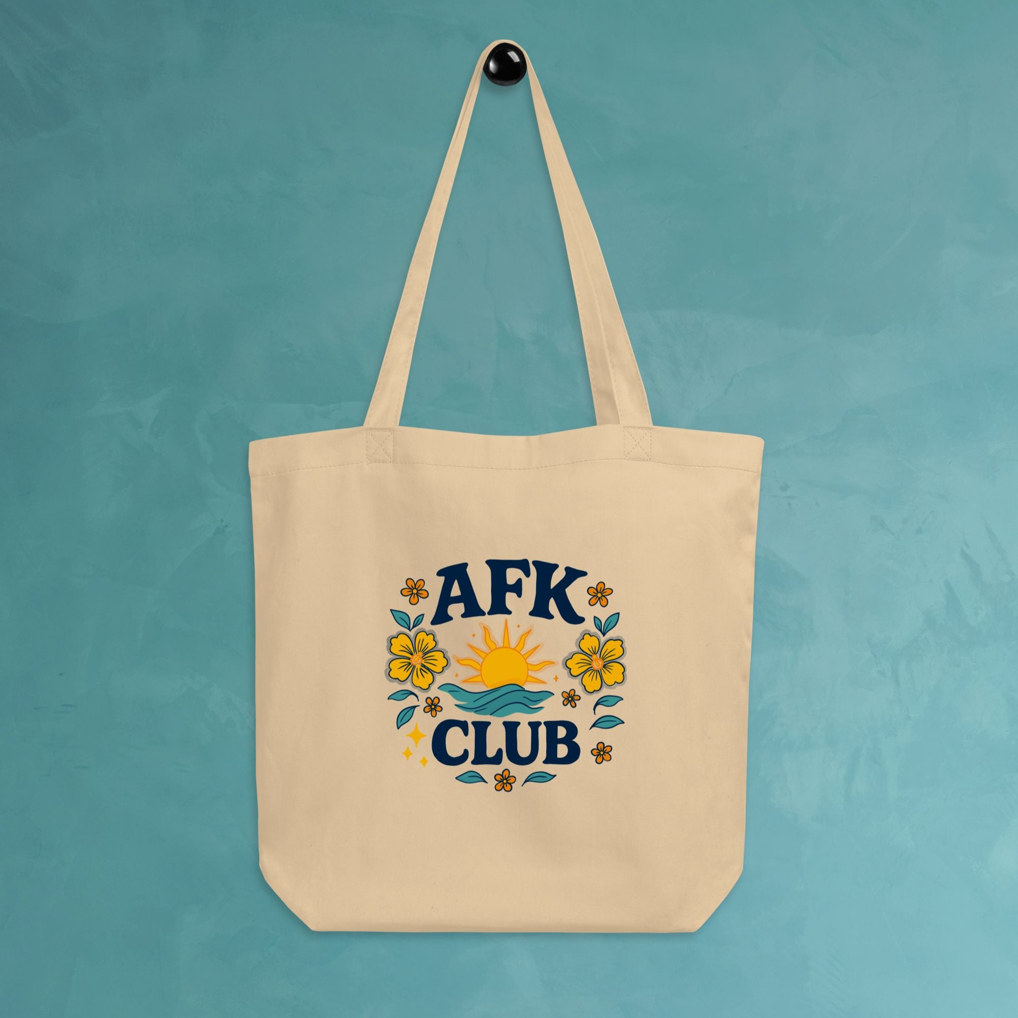 Beige tote bag with 'AFK Club' design hanging on a teal wall.