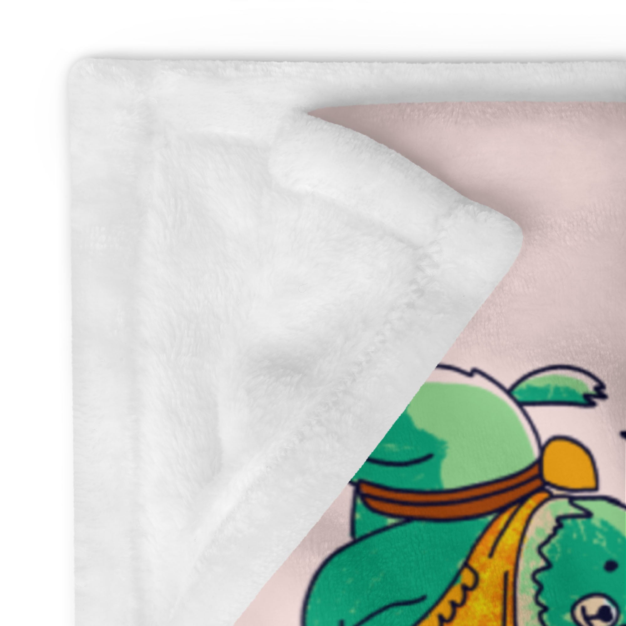Close-up of a folded throw blanket corner revealing soft white fleece backing and pastel-pink front print featuring a green cartoon bear from the Dream Big Adventure Animals design.
