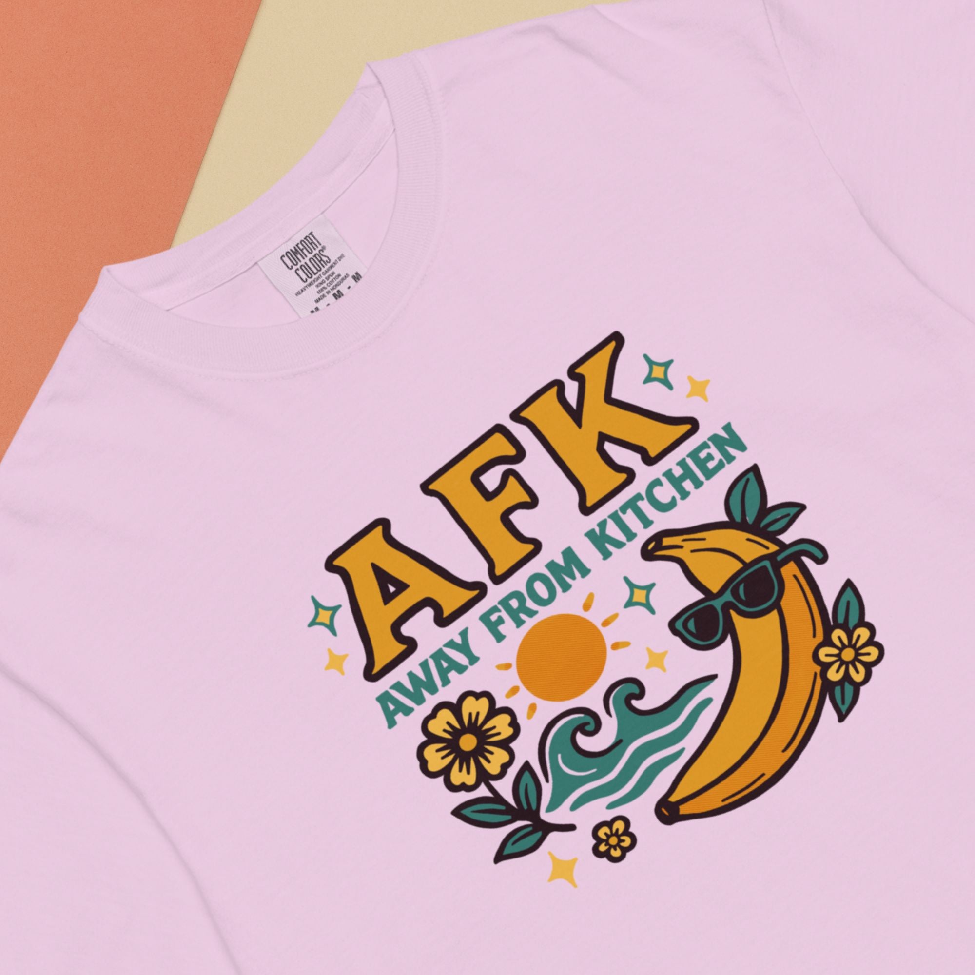 Pink t-shirt with 'AFK Away From Kitchen' graphic design featuring a banana and flowers on a multicolored background.