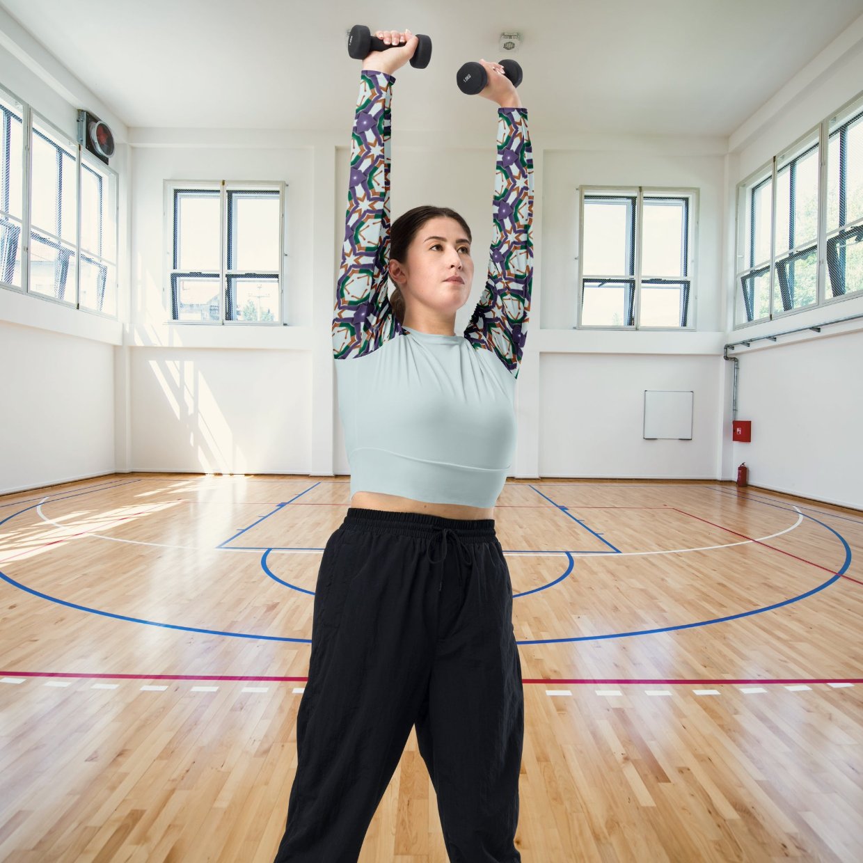 Woman wearing Recycled Long-Sleeve Crop Top in Soccer Star, lifting weights, showcasing the soccer-inspired patterned sleeves and wide waistline band.