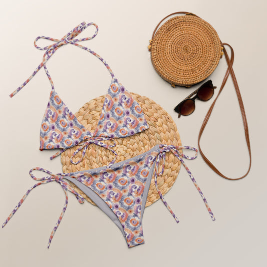 Recycled string bikini with a dreamy tie-dye pattern in lavender, peach, and cream, featuring adjustable ties and eco-friendly materials.