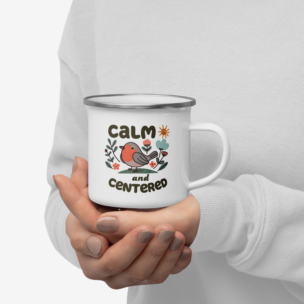 Person holding a white mug with a design of a bird and text 'CALM and CENTERED' on a plain background