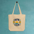 Beige tote bag with 'AFK Club' design hanging on a teal wall.
