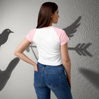 Woman wearing a white and pink shirt with blue jeans, standing against a gray wall with shadow effects.
