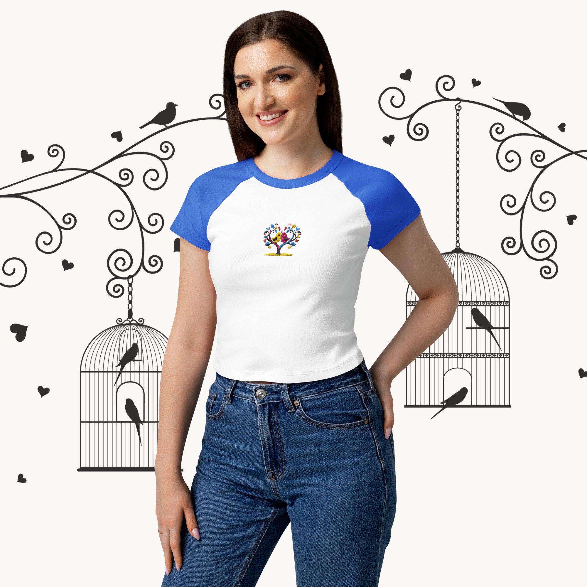 Woman wearing a white and blue baseball shirt with a colorful design, standing against a decorative background with birdcages and birds.