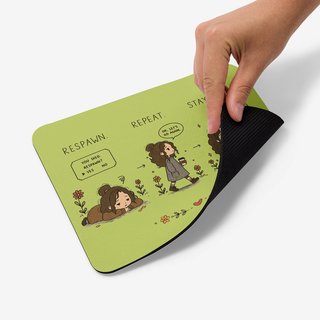A hand is showing the back by a corner of a light green mousepad with a black textured underside. The top surface features a cartoon illustration of a girl and a dog with text including 'RESPAWN.REPEAT.STAY ZEN.'
