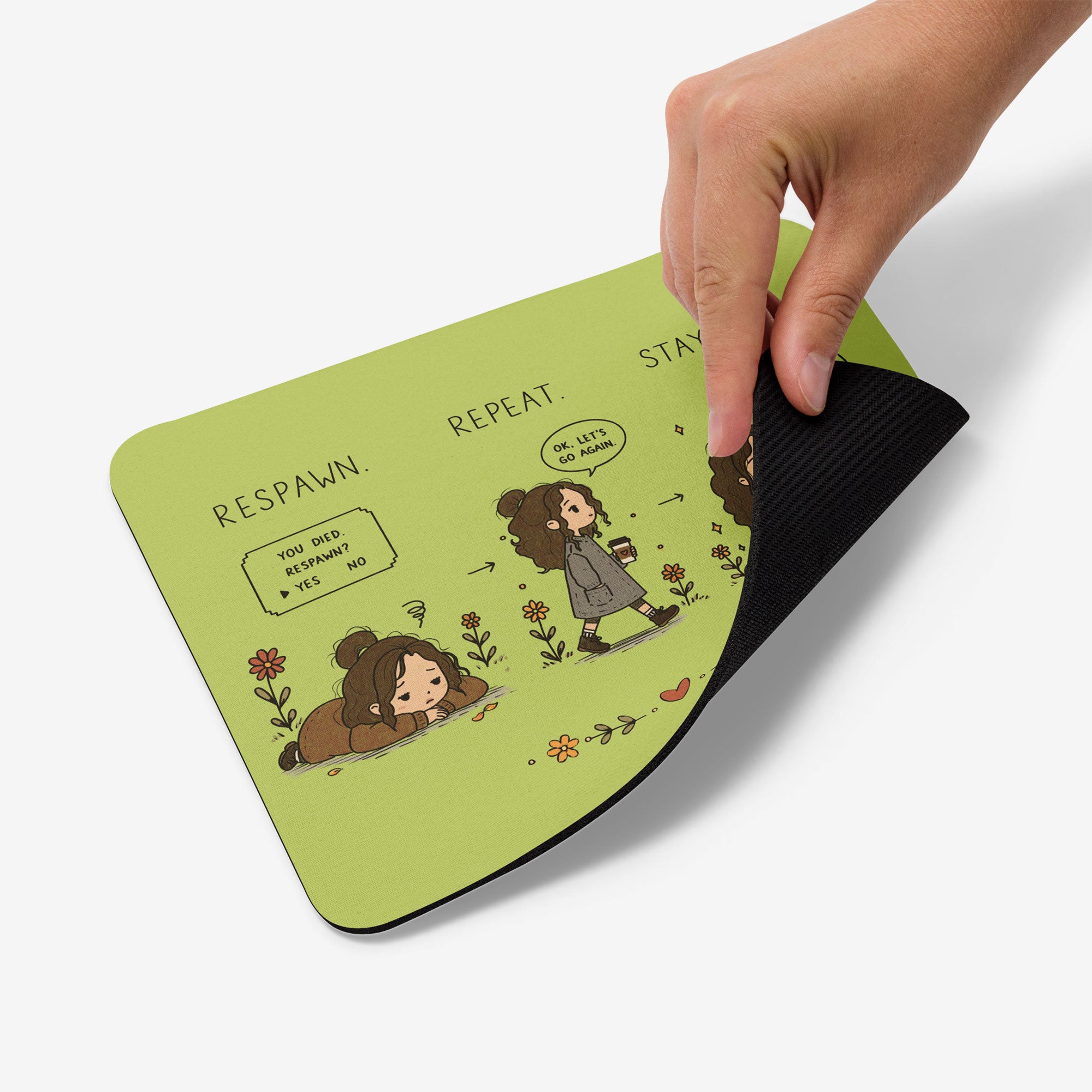 A hand is showing the back by a corner of a light green mousepad with a black textured underside. The top surface features a cartoon illustration of a girl and a dog with text including 'RESPAWN.REPEAT.STAY ZEN.'