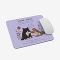 A lavender rectangular mouse pad with rounded corners, featuring a printed illustration of a black cat and a robin bird with the text “THERE THERE” and a quote. A white computer mouse rests on the right side of the pad against a light gray background.