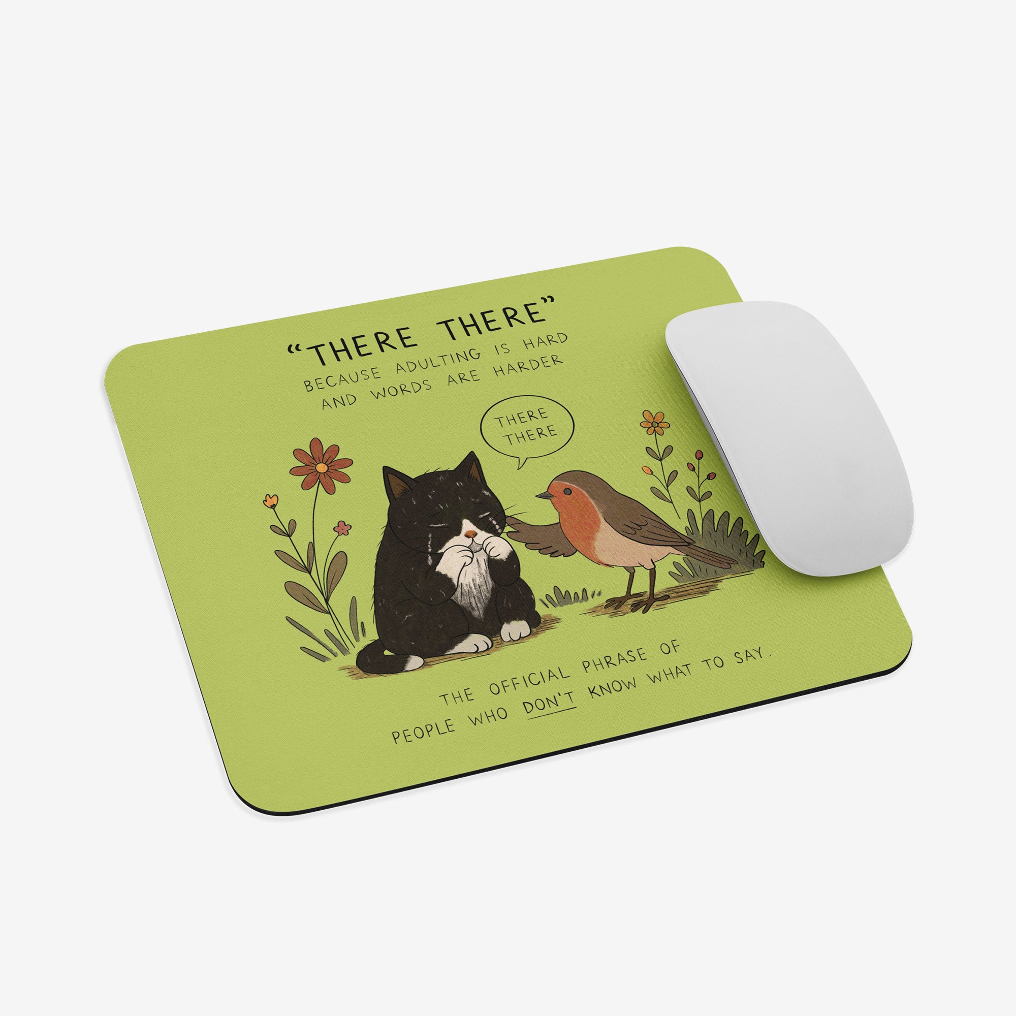 A rectangular mousepad with rounded corners on a light gray background, featuring a lime green base with a cartoon illustration of a black cat and a red-breasted bird with the text “THERE THERE.” A white computer mouse rests on the right side of the pad.