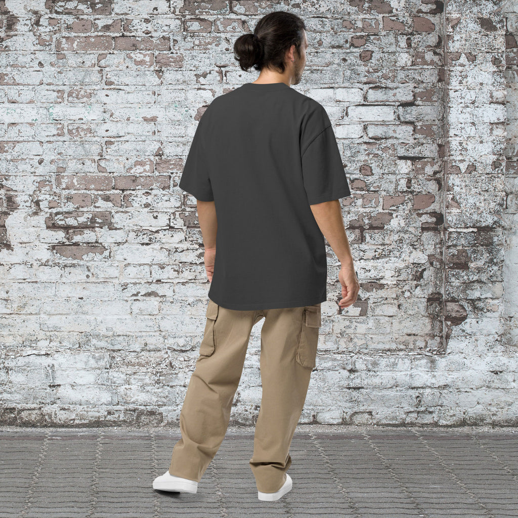 Person wearing a dark gray t-shirt and beige cargo pants standing against a textured brick wall.