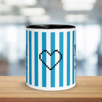 Mug with blue and white striped design and black pixelated heart symbol on a wooden surface.
