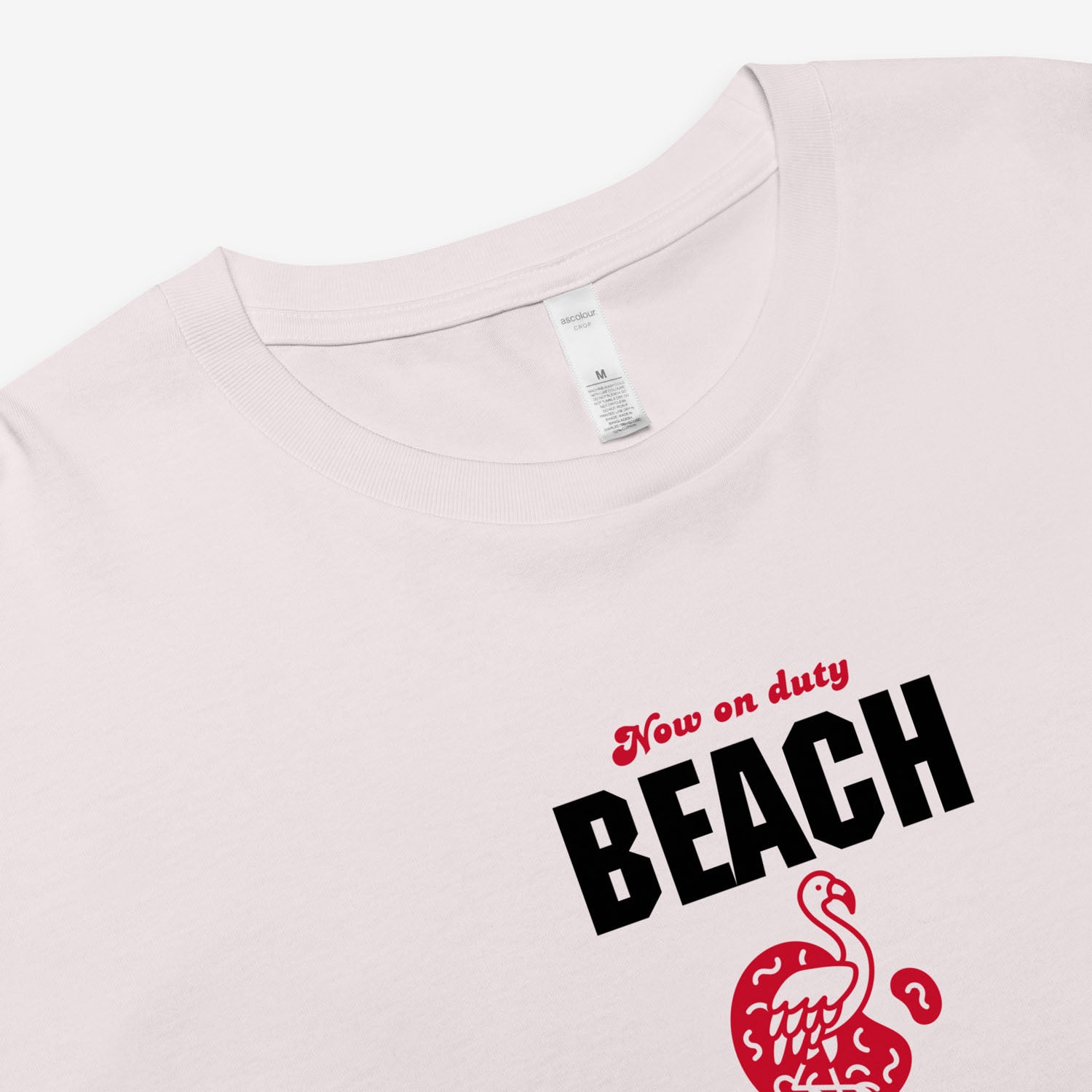 Light pink t-shirt with 'Now on duty BEACH' text and flamingo graphic on a white background closeup tag 