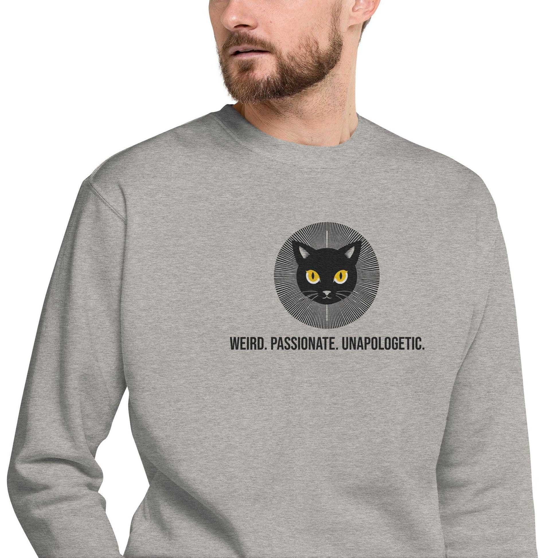 man in grey sweatshirt, right front view, zoomed on the embroidered design of a black cat with yellow eyes embroidery radiating confidence and the erdegora tag line Weird. Passionate. Unapologetic